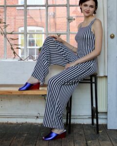 Marla in Ops&Ops No15 Metallic Purple wedge mules worn with striped, strappy jumpsuit