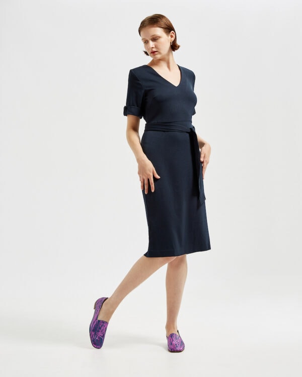 Marla in Ops&Ops No17 Woodland Blue flats with belted navy blue dress, looking over her shoulder