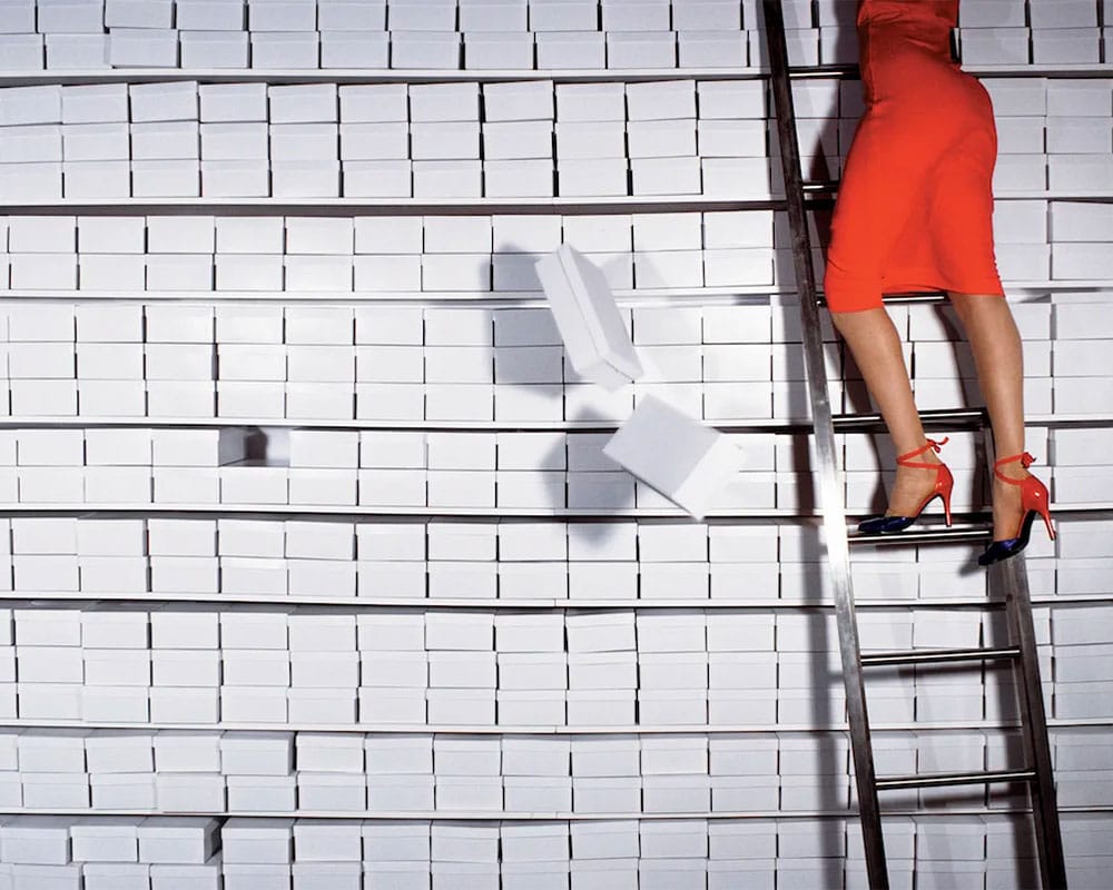 Guy Bourdin 77, woman on a ladder against a wall of shoe boxes